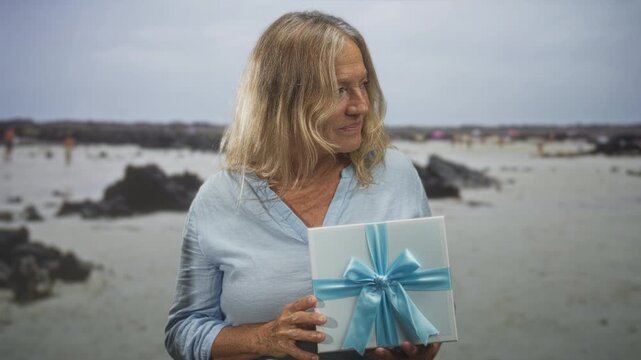 Woman holds white gift box tied with blue ribbon, right hand supports box and left hand touches bow, studio setting; serenity gratitude.