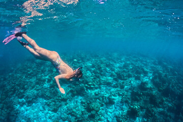 Female freediver exploring coral reef in clear tropical ocean. Woman snorkeling above colorful seabed with fins and mask, underwater travel adventure and marine nature exploration.