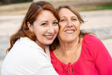 Obraz premium Daughter embracing her elderly mother outdoors, both women smiling and showing strong connection and affection