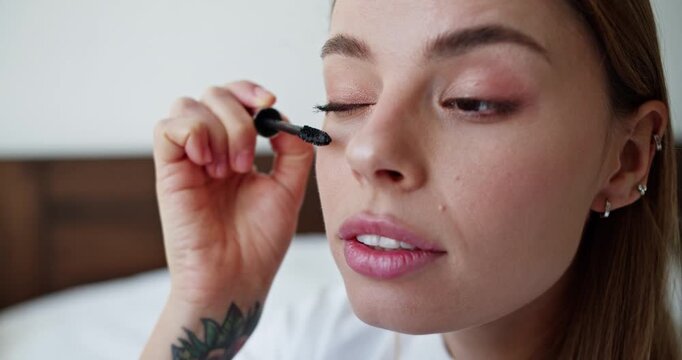 Young woman applying mascara for a daily makeup beauty routine in her bedroom