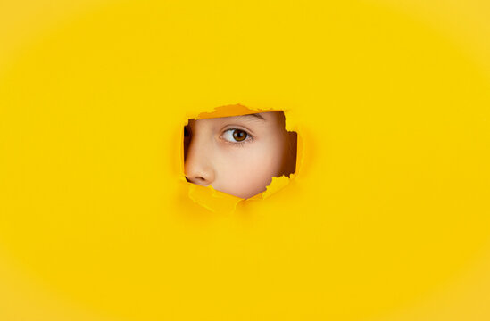 Spying, spy on or overhearing the concept. Spy eye watching through hole. Child's eye looking throughs hole. Boy breaks paper. Boy peeks through a cut hole in red paper wall. Human eye closeup
