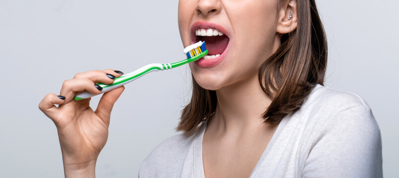 Happy girl brushing her teeth. The concept of a healthy lifestyle. Dental hygiene. Smiling young woman with healthy teeth holding a tooth brush. Young beautiful girl holding a toothbrush