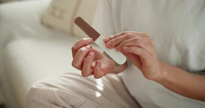 Woman filing nails with emery board during home manicure routine on a sunny morning