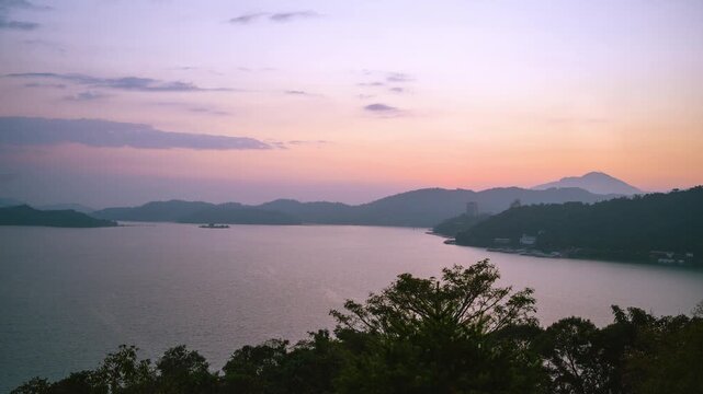 A serene sunset view over the tranquil waters of Sun Moon Lake in Nantou, Taiwan, featuring silhouettes of mountains and lush trees.