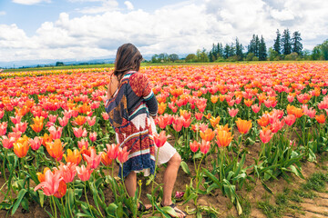 A woman stands in a field of flowers, wearing a colorful jacket and shorts © ExploringandLiving