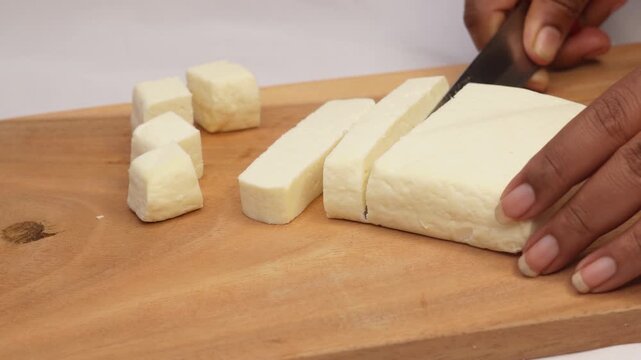 Woman cutting healthy homemade paneer or tofu milk cheese on wooden cutting board. The product is ready to use. White background.