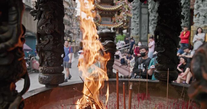 New Taipei City, Taiwan, May 12, 2025: The blazing flames of incense burners in a traditional temple create a dynamic contrast with the crowds of people praying and the magnificent dragon pillar carvi