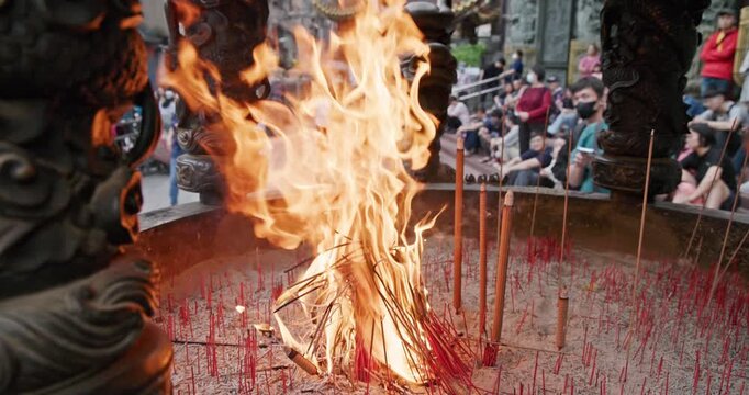 New Taipei City, Taiwan, May 12, 2025: The blazing flames of incense burners in a traditional temple create a dynamic contrast with the crowds of people praying and the magnificent dragon pillar carvi