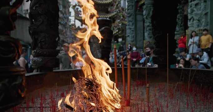 New Taipei City, Taiwan, May 12, 2025: The blazing flames of incense burners in a traditional temple create a dynamic contrast with the crowds of people praying and the magnificent dragon pillar carvi