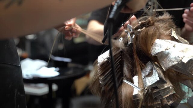 Professional hairstylist using a blow dryer on a section of hair during a complex foiling and coloring treatment