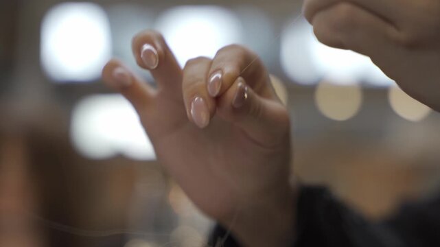 Extreme close up of a stylist's hand delicately holding a single strand of hair for extension application