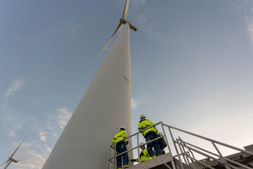Wind turbine engineer and technicians standing on service platform inspecting wind turbine tower at renewable energy farm. Clean electricity generation, sustainable power industry concept.