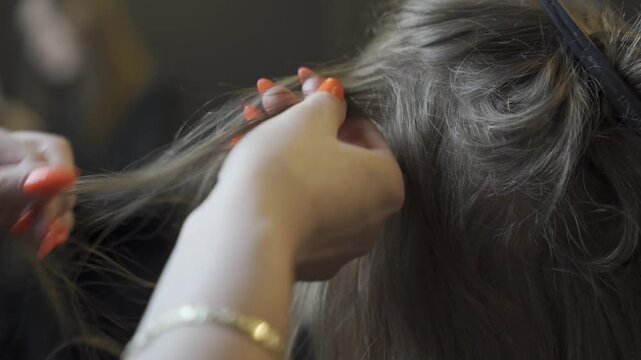 Hairdresser with bright orange nails using a comb to section hair for the application of professional hair extensions. Extreme close up