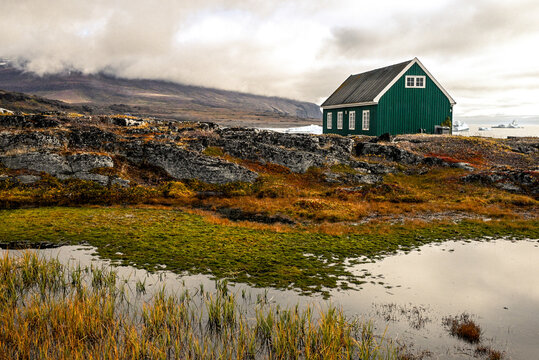 Qeqertarsuaq, Disko Island, Greenland - Colorful seascape featuring a charming green cottage on a rainy, fall day