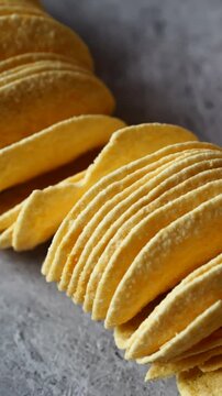 A long row of yellow potato chips is neatly stacked, gradually becoming a casual pile on a distressed grey surface, ready to eat.
