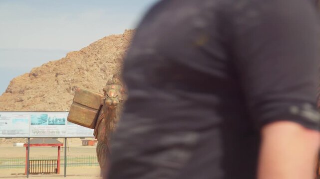 Desert Caravan Camels Carry Wooden Crates Along Sunlit Roadside With Rocky Mountain Backdrop, Luggage Strapped To Saddles, Slow Paced Nomadic Transport Scene With Warm Tones And Rugged Travel Mood