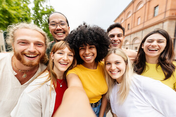 Fototapeta premium Young multiracial group of friends taking selfie outdoors. Happy young people smiling together in an urban European setting. Community and lifestyle concept.