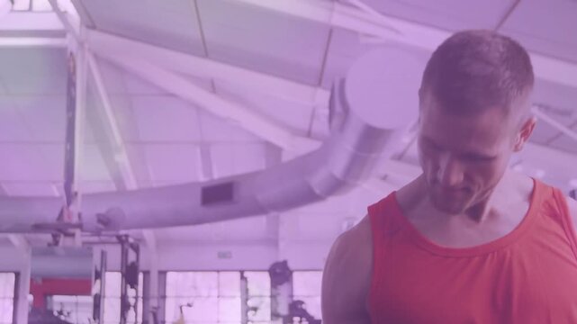 Curling mid-adult man in red tank top lifting adjustable dumbbell in large gym, copy space