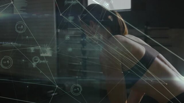 Pulling mid-adult woman wearing dark sports bra in gym training area, with HUD, dumbbell