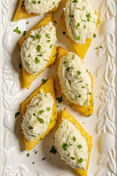 Top view of baccala mantecato, whipped, creamed salt cod fish spread, is a Venetian appetizer made with dried cod, served on fried polenta croutons. Verttical image.