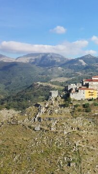 Scenic view of the historic hilltop village of Aieta, Italy, surrounded by terraced fields and mountains under a clear blue sky.
