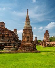Fototapeta premium Ancient stupa towers in Ayutthaya historical park, Thailand. Ruins of former Siam capital under blue sky on sunny day. Famous travel destination with cultural heritage and Buddhist history.