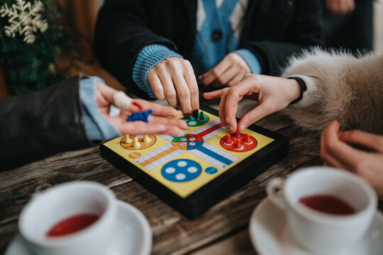 Girls play a colorful board game on a wooden table with tea cups nearby; a warm, casual moment of togetherness.