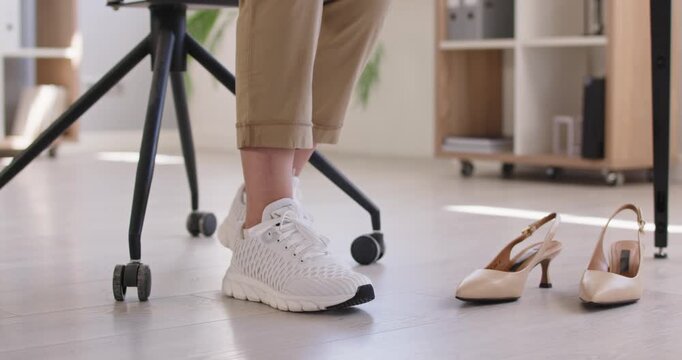 Change from shoes with heels to sneakers for women feet comfort in office workplace. Comfy footwear choice of young woman sitting in chair at desk, tired legs health support for businesswoman