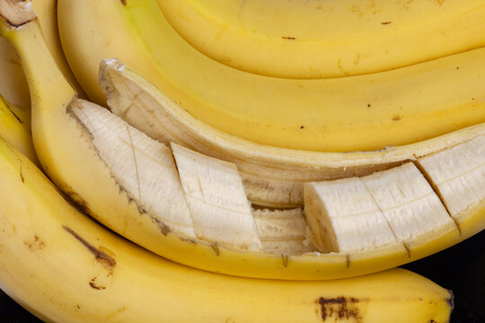 Close up on bunch of ripe yellow bananas in black bowl, one partially pilled and cut in to slices