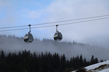 Cable Car Gondolas Above Misty Alpine Forest with Breaking Clouds © Niki