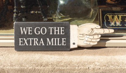 Support, help we go the extra mile symbol. Concept words We go the extra mile on beautiful wooden black sign. Beautiful store front background. Business we go the extra mile concept. Copy space.