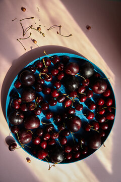 Still life of cherries and plums in blue bowl with window light.