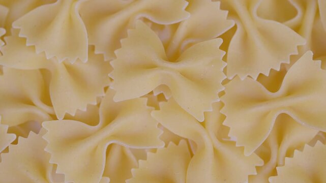 Uncooked bow tie pasta detail. Closeup of pale uncooked bow pasta with soft lighting. Detailed view of pale golden farfalle pasta with subtle texture and warm highlights