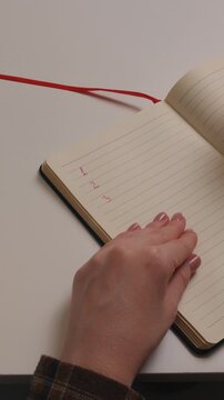 Close-up of a hand writing a numbered list in a notebook. Person writing tasks one, two, three