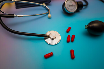 A professional still life featuring a medical stethoscope, a tonometer, and bright red capsules on a rich blue background illustrates the concept of cardiovascular health.