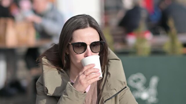 Stylish Woman Wearing Sunglasses Drinking Coffee Outdoors At Cafe. Female Relaxing With Hot Drink In Urban Environment On Cool Day. Leisure Lifestyle And City Coffee Break Concept Video.