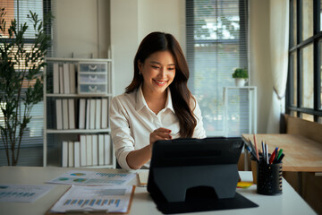 Asian businesswoman smiling, working on tablet, analyzing data in a modern office setup