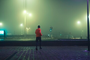 Under the soft glow of streetlights, a dedicated runner explores the quiet urban landscape. The fog...