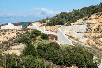 Unfinished dam construction in mountainous landscape showing concrete spillway structure, engineering infrastructure project and environmental impact.