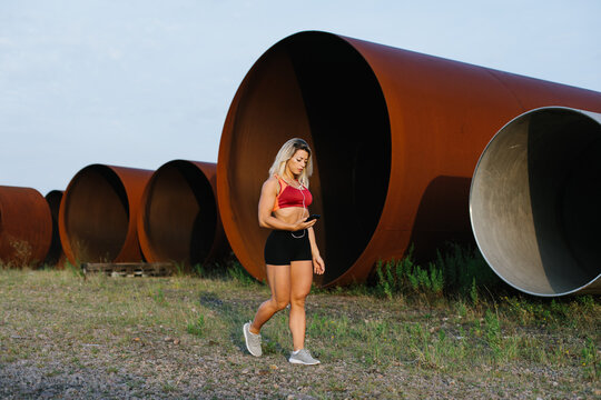 Full length photo of a female athlete walking while taking a workout break to play music on her smartphone. 