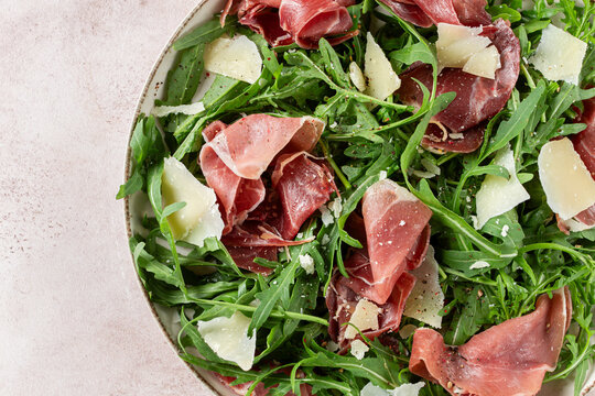 Fresh arugula salad with prosciutto and grated parmesan cheese, on a plate, homemade, no people,