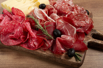 Assorted meat, appetizer, prosciutto, salami and ham, with maasdam cheese and olives, on a wooden...