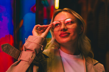 Woman adjusting glasses under vivid colored lights