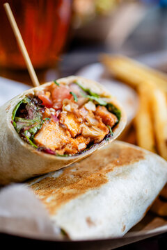 A buffalo chicken wrap with tomatoes lettuce red onion served with fries at a modern restaurant and cafe 