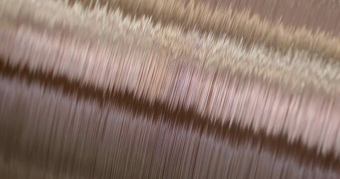 A cable-making machine is in operation. A spool of copper wire is rotating. Close-up handheld shot, real time speed.