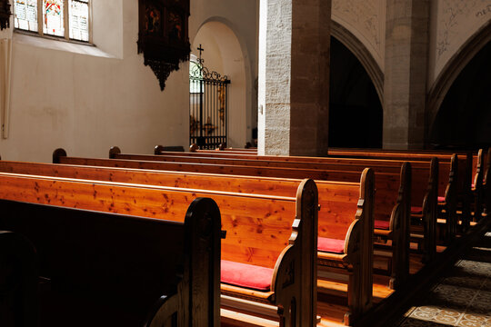 Rows of traditional carved wooden pews create a perspective view inside a historic church in Austria, showcasing sacred architecture and quiet devotion. Stock photo