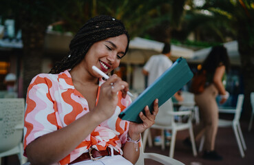 Young woman smiling while drawing on digital tablet outdoors, highlighting creativity, optimism, and the powerful connection between art and technology in modern mobile lifestyles.