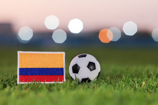 Colombia flag and soccer ball on night stadium grass. Cinematic bokeh background, symbolic for international football tournaments, national pride, and South American sports.