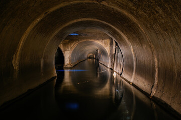 Fototapeta premium Inside underground urban sewer system. Dirty sewage flowing in round sewer pipe