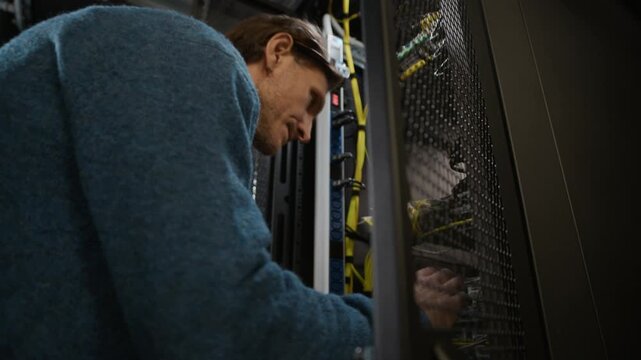 Close up low angle shot of data center engineer working inside server rack, connecting network cables and checking hardware equipment in modern information technology infrastructure environment